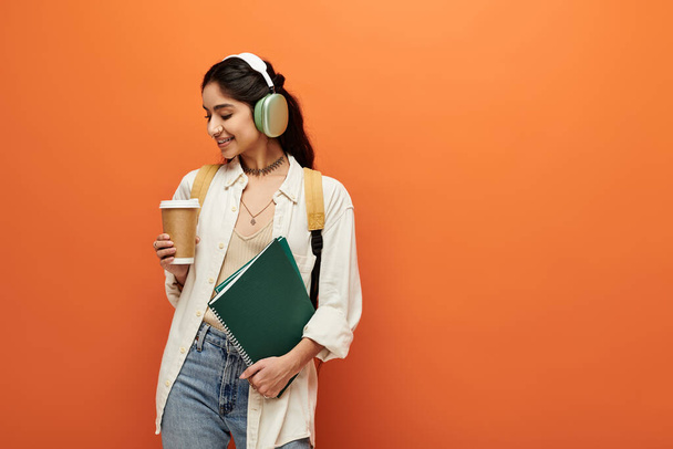 Fiatal indiai nő élvezi a zenét fejhallgatóval, miközben a kezében egy csésze kávé. - Fotó, kép