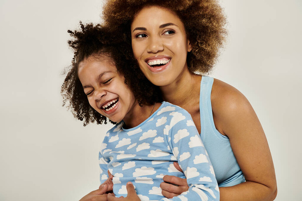Szczęśliwa Afroamerykanka w piżamie przytula córkę delikatnie przed białym tłem. - Zdjęcie, obraz