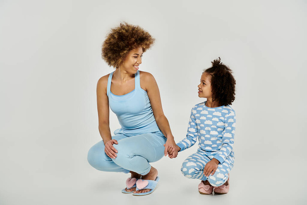 Счастливые афроамериканская мать и дочь в одинаковых пижамах, разделяя радостный момент на белом фоне. - Фото, изображение
