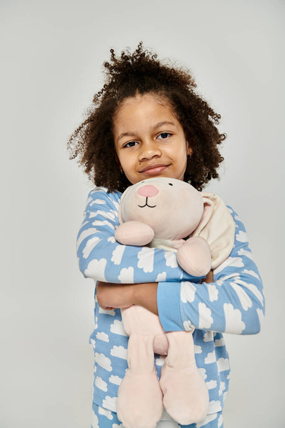 An African American girl in pajamas joyfully holds a stuffed animal - Photo, Image