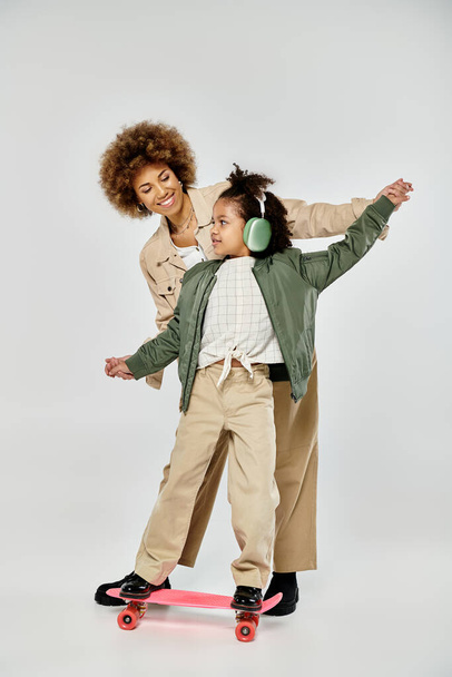 Кучерява афроамериканська мати і дочка в стильному одязі впевнено катаються разом на сірому фоні. - Фото, зображення
