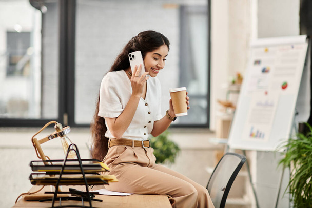 Μια νεαρή Ινδή κάθεται σε ένα γραφείο, απορροφημένη σε μια τηλεφωνική συνομιλία.. - Φωτογραφία, εικόνα