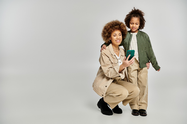 Кучерява афроамериканська мати і дочка в стильному одязі, що вражає позу разом на сірому фоні. - Фото, зображення
