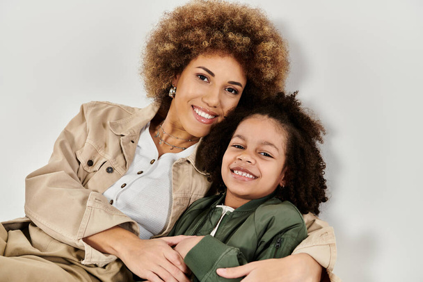 Madre e hija afroamericana rizada con ropa elegante posando juntas sobre un fondo gris. - Foto, imagen