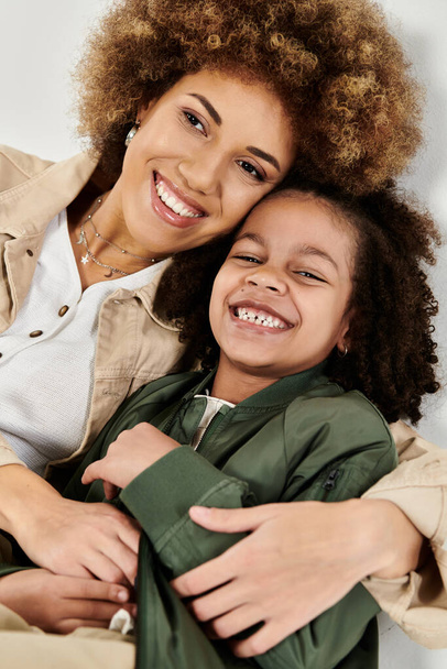 Kıvırcık Afrikalı Amerikalı anne ve kız şık kıyafetler içinde beyaz bir arka planda birbirlerine sarılıyorlar.. - Fotoğraf, Görsel