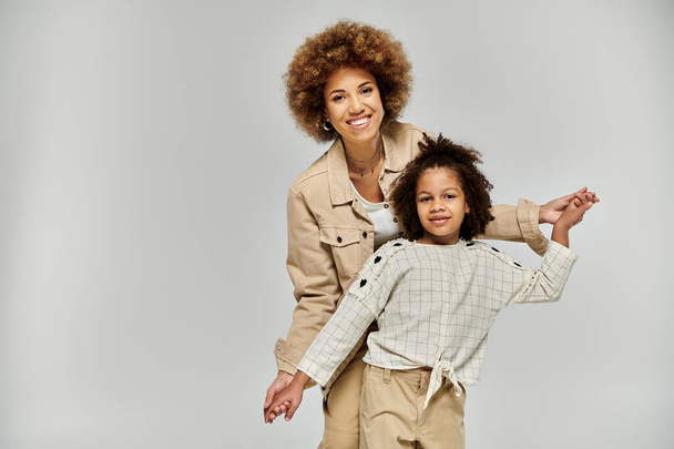 アフリカ系アメリカ人の母親と娘,スタイリッシュな服装で,灰色の背景にポーズを打つ. - 写真・画像