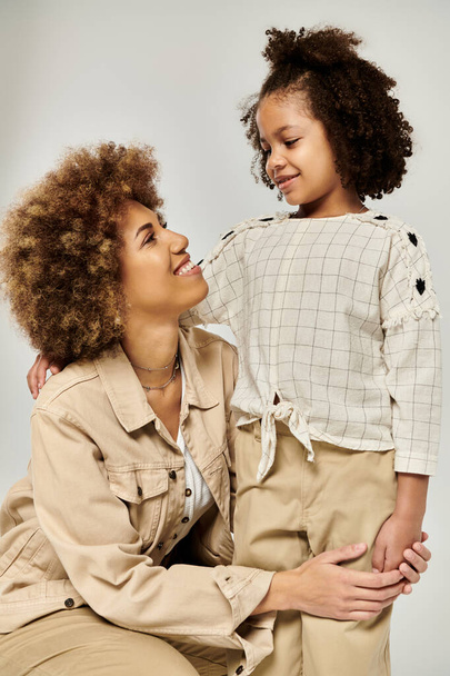 Стильные кудрявые афроамериканская мать и дочь, ставящие вместе позу на сером фоне. - Фото, изображение