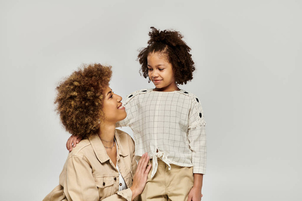 Egy göndör afro-amerikai anya és lánya elegáns ruhákban, elegánsan pózolnak szürke alapon.. - Fotó, kép