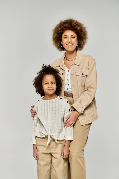 Lockige afroamerikanische Mutter und Tochter posieren stilvoll vor neutralem grauen Hintergrund. - Foto, Bild