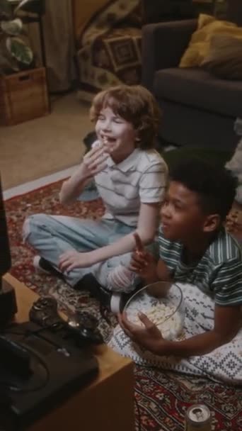 Imágenes verticales de alto ángulo de dos chicos felices y diversos sentados en el suelo frente a la vieja televisión de tubo y viendo películas en casa, atmósfera de nostalgia de los años 90 - Metraje, vídeo