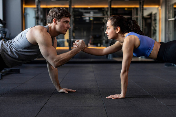 Fit sportive man and woman doing plank core exercise in the gym, and standing on one hand, giving high five to each other, side view - Photo, Image
