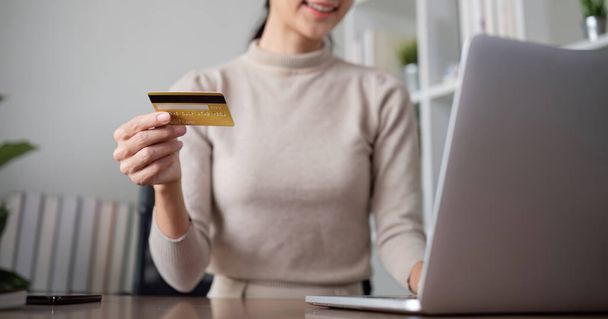 Красива молода жінка використовує ноутбук для покупки в Інтернеті, купує речі і платить за допомогою кредитної картки через додаток онлайн-банкінгу.. - Фото, зображення
