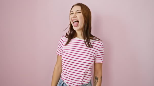 Fun-loving young brunette girl in striped tshirt, sticking tongue out with a happy amusement, over pink isolated background. joyful expression radiating crazy positivity. - Footage, Video