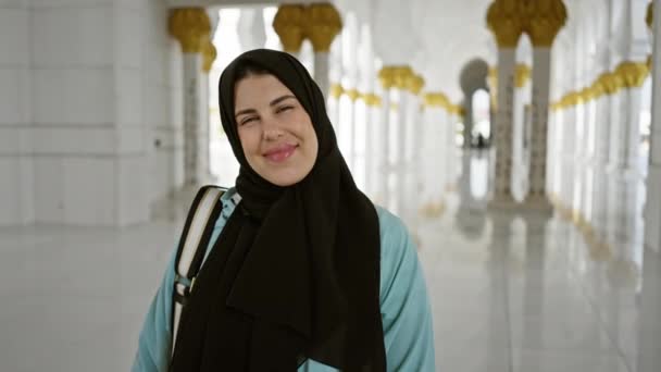 Glimlachende vrouw met hijab in de sierlijke gang van een moskee in abu dhabi - Video