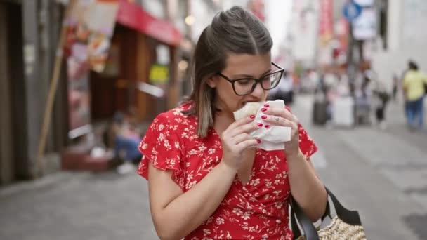 A gyönyörű spanyol nő megízleli az Oszaka híres dotonbori utcájában lévő finom rákhúsos zsemlét, szemüvege tükrözi a város vibráló fényeit. - Felvétel, videó