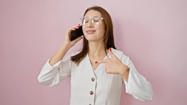Cheerful young brunette girl joyfully gesturing an idea with a confident smile while on phone, speaking with bright emotion, pointing finger against isolated pink backdrop, lost in happy conversation - Footage, Video