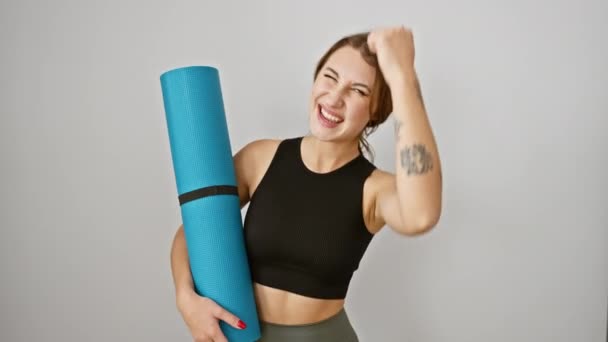 Excited young brunette girl in sportwear celebrates victory! proudly holds yoga mat, arms raised in triumph, isolated on white background. - Footage, Video