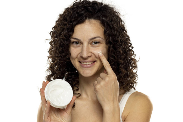 Ritratto di una giovane donna attraente applicare un prodotto di bellezza sul suo viso su uno sfondo bianco studio. - Foto, immagini
