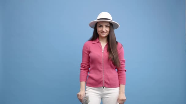 Frau in legerer Kleidung und weißem Hut mit Reisepass und rotem Koffer auf blauem Hintergrund. Flugreise-Konzept - Filmmaterial, Video