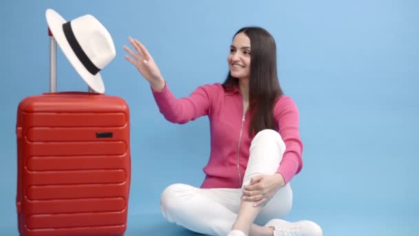 Gelukkig jong toeristisch vrouw zitten aan de koffer en gaan reizen op vakantie geïsoleerd op blauwe achtergrond - Video