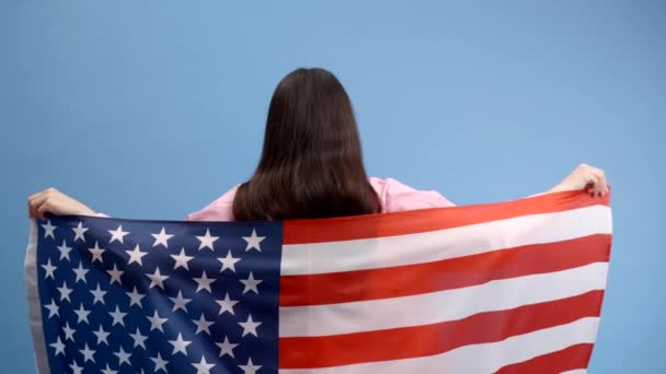 Giovane donna felice sorridente indossa abiti casual con bandiera americana e guardando la fotocamera isolata su sfondo di colore blu - Filmati, video