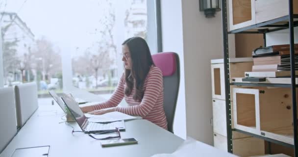 В офісі молода жінка зосереджена на аналізі зростання бізнесу, доходів та прибутку на своєму комп'ютері, оточеному паперовими роботами, демонструючи свою відданість досягненню успіху бізнесу. - Кадри, відео