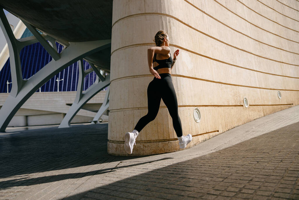 Mujer joven en ropa deportiva se ejecuta en los edificios modernos de fondo. Concepto de estilo activo - Foto, imagen