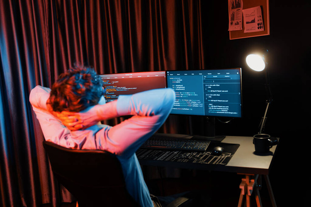 Pracujący programista IT koncentrujący informacje o rozwoju oprogramowania online na otoczony przez kodowanie aplikacji ekranów komputerowych, tworząc program dla oprogramowania firmowego na stronie internetowej w neon nowoczesny dom biurowy. Pędziwiatr. - Zdjęcie, obraz