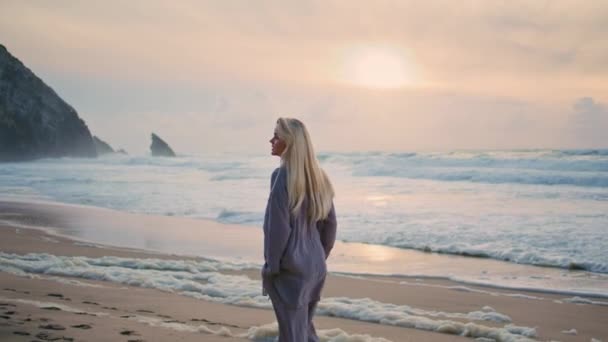 Dziewczyna spacerująca o zachodzie słońca latem. Szczęśliwa turystyczna kamera wirująca ciesząca się podróżą na wakacje. Piękna kobieta idzie zachmurzone wybrzeże patrząc niesamowite piankowe fale. Radosna blondynka odpoczywająca na wyspie Cliff - Materiał filmowy, wideo