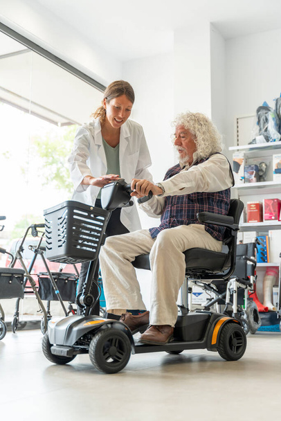 Oudere man in een orthopedische producten winkel proberen een elektrische scooter - Foto, afbeelding