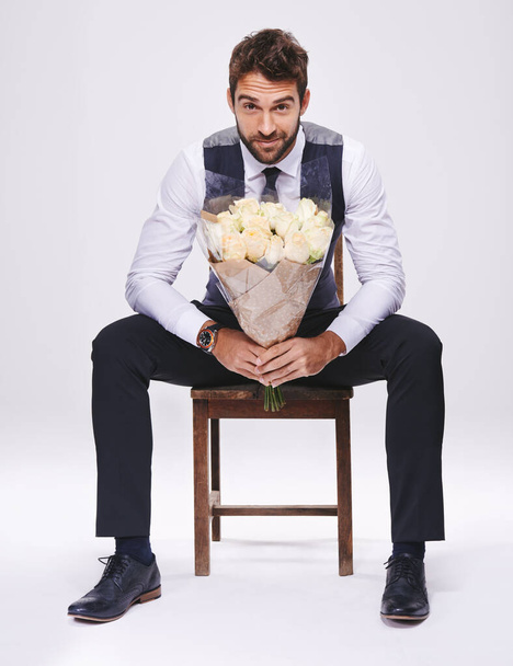 Studio, portrait and man with chair, bouquet and date for style and fashion. Gentleman, designer and romance with flowers, confidence and proud ambition with suit isolated on white background. - Photo, Image