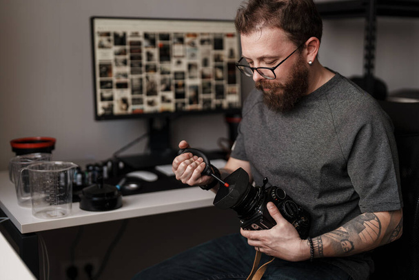 Gericht mannelijk fotograaf zorgvuldig schoonmaken van de lens van een professionele camera op zijn georganiseerde, hedendaagse werkplek. - Foto, afbeelding