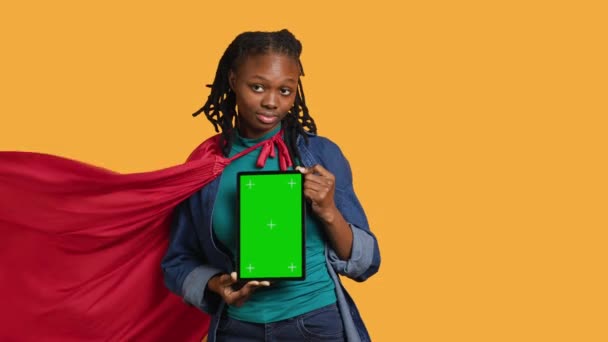 Ritratto di donna gioiosa raffigurante supereroe che mostra tablet schermo verde, dando feedback positivi, sfondo dello studio. Persona radiante che fa cosplay eroe raccomandando dispositivo mockup, fotocamera A - Filmati, video