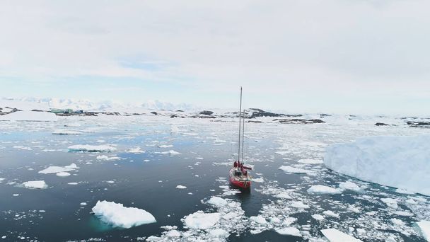 Żeglarstwo Jacht Podróż na Antarktydzie Spokojny Brash Ocean lodowy wśród Iceberg Aerial Tracking. Red Boat Poznaj efekt globalnego ocieplenia w krajobrazie przyrody polarnej Top Drone View - Zdjęcie, obraz