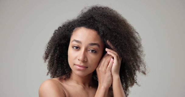 Beauty and Healthcare concept - Beautiful African American woman with curly afro hairstyle hair and clean, healthy skin on gray studio background posing and looking at camera. - Fotografie, Obrázek
