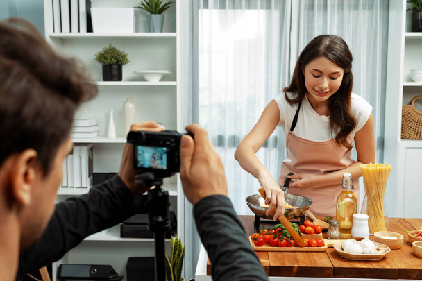 シェフのインフルエンサーの女性にカメラマンレコーディング ホストは,トマトソースをトッピングスパゲッティをトッピングし,食材レシピを取り囲み,現代のスタジオで特別な料理健康食品を提示します. ポストレート. - 写真・画像