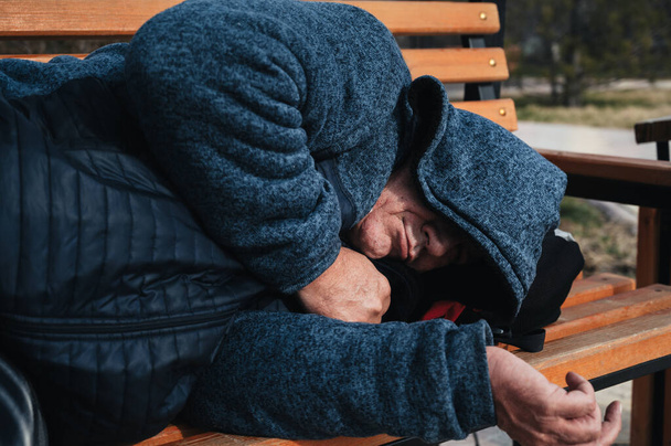 Obdachloser alter Kaukasier liegt im Herbst schlafend auf einer Parkbank - Foto, Bild
