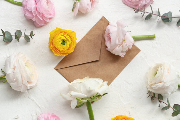 Okaliptüslü güzel ranunculus çiçekleri ve beyaz grunge arkaplanlı zarf. - Fotoğraf, Görsel