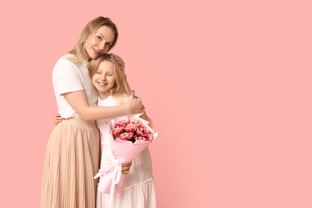 Nettes kleines Mädchen mit Blumenstrauß zum Muttertag umarmt ihre Mutter auf rosa Hintergrund - Foto, Bild