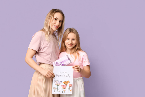 Cute little girl giving gift box and festive postcard her mom for Mother's Day on lilac background - Photo, Image