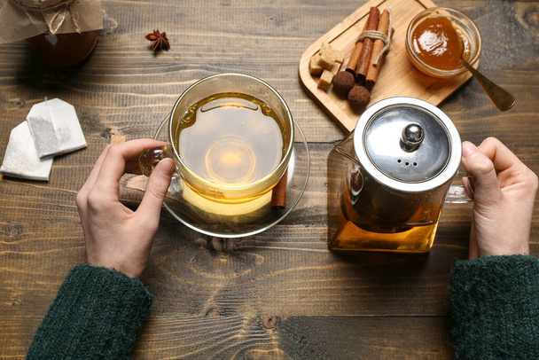 Γυναικεία χέρια που κρατούν τσαγιέρα και φλιτζάνι τσάι κανέλας σε ξύλινο φόντο, κοντινό πλάνο - Φωτογραφία, εικόνα