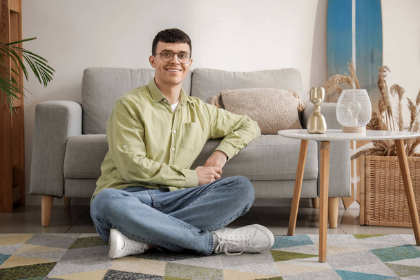 Schöner junger Mann mit neuer stylischer Brille sitzt zu Hause auf dem Fußboden - Foto, Bild