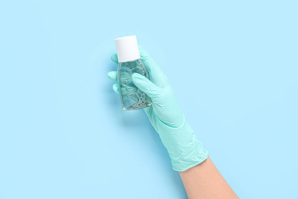 Жіноча рука в рукавичках з пляшкою дезінфікуючого засобу на синьому фоні - Фото, зображення