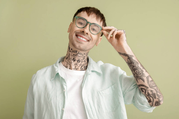 Молодой татуированный мужчина в очках на зеленом фоне, крупным планом - Фото, изображение
