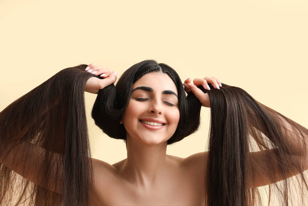 Hermosa joven feliz mujer con cabello largo saludable sobre fondo beige - Foto, Imagen