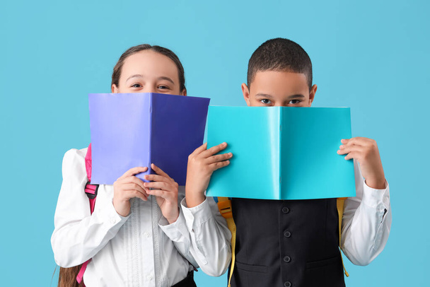Glückliche kleine Schüler mit Rucksäcken und Heften auf blauem Hintergrund - Foto, Bild