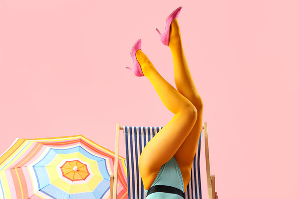 Πόδια της όμορφης νεαρής γυναίκας με ξαπλώστρα και ομπρέλα σε ροζ φόντο - Φωτογραφία, εικόνα