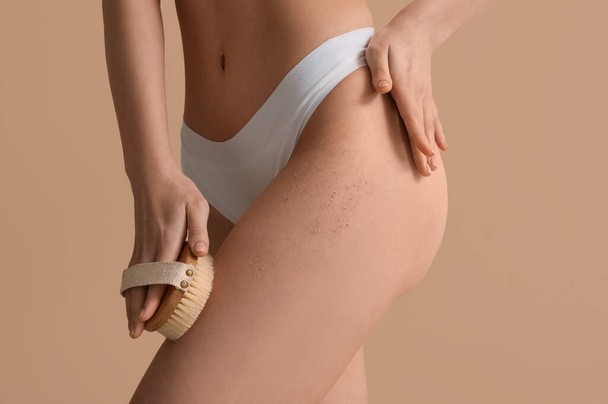 Junge Frau mit Massagebürste schrubbt Bein auf beigem Hintergrund - Foto, Bild
