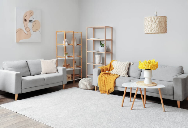 Gemütliche Sofas, Regal und Couchtisch mit Narzissenblumen-Vase im Wohnzimmer - Foto, Bild