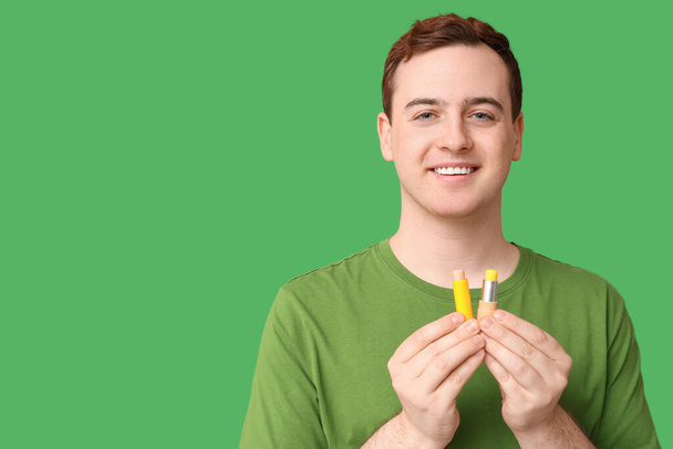 Handsome young man with lip balms on green background - Photo, Image